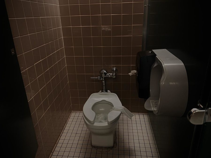 This stall is missing equipment and its toilet is overflown with toilet paper.