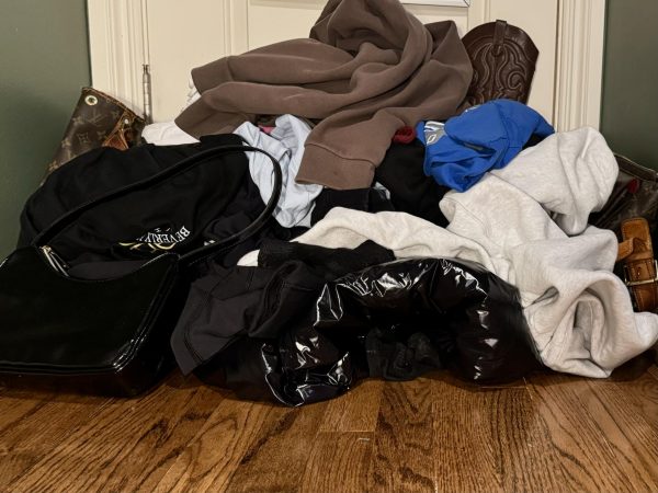 Mountain of clothes, bags, jackets, and shoes stacked on the floor.