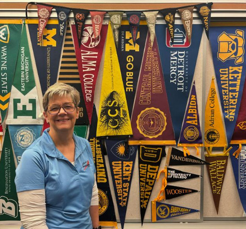 	Mrs.Kondak stands proudly in front of college banners tacked on her office wall. 