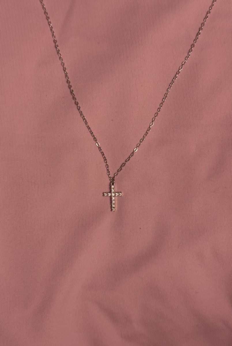 A silver, sparkling cross laid against a pink background.