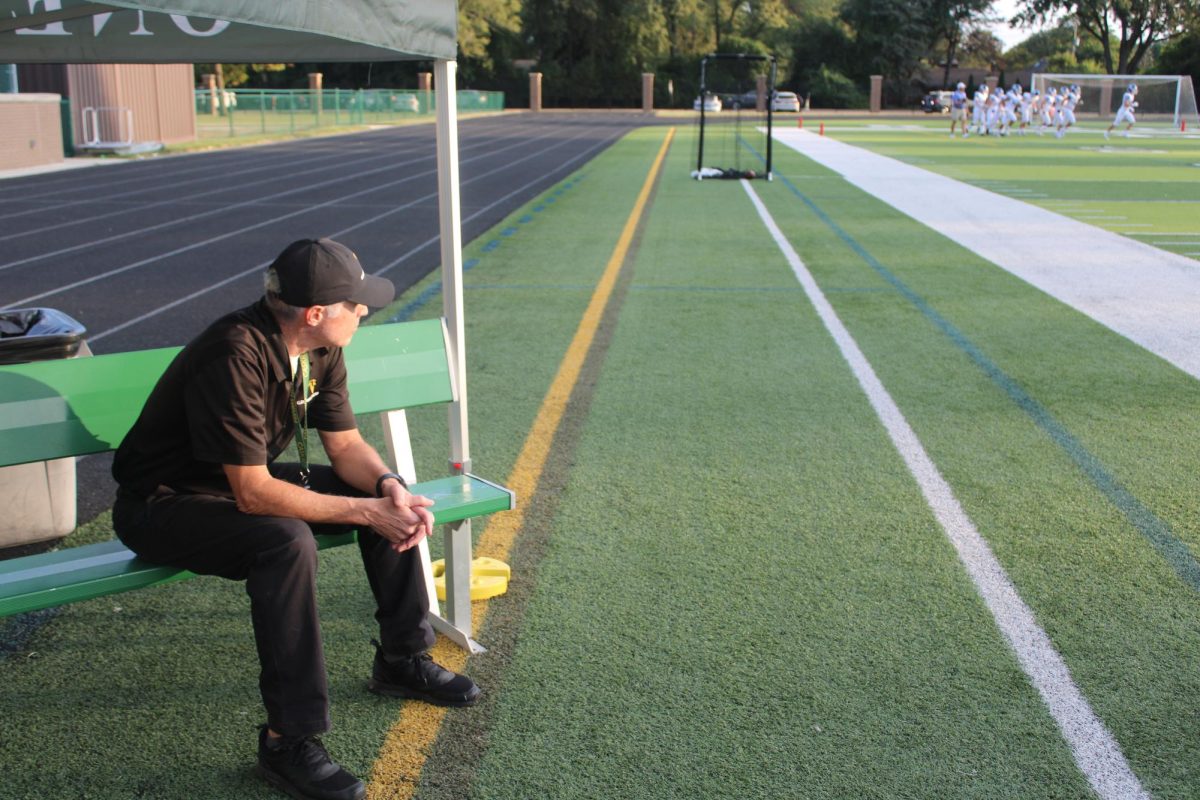 Groves football coach sits on the sideline bench, preparing for the upcoming game. 