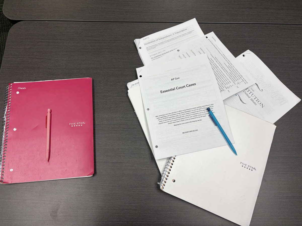 A desk with one side having a notebook and pencil, and the other side having multiple papers, a notebook and a pencil representing the amount of work AP classes can be for students.