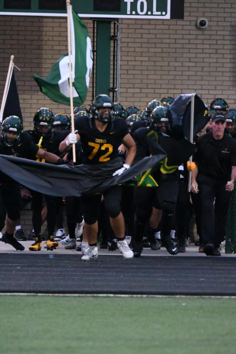 The Groves Varsity Football Team charges the field holding a Groves Football Flag.
